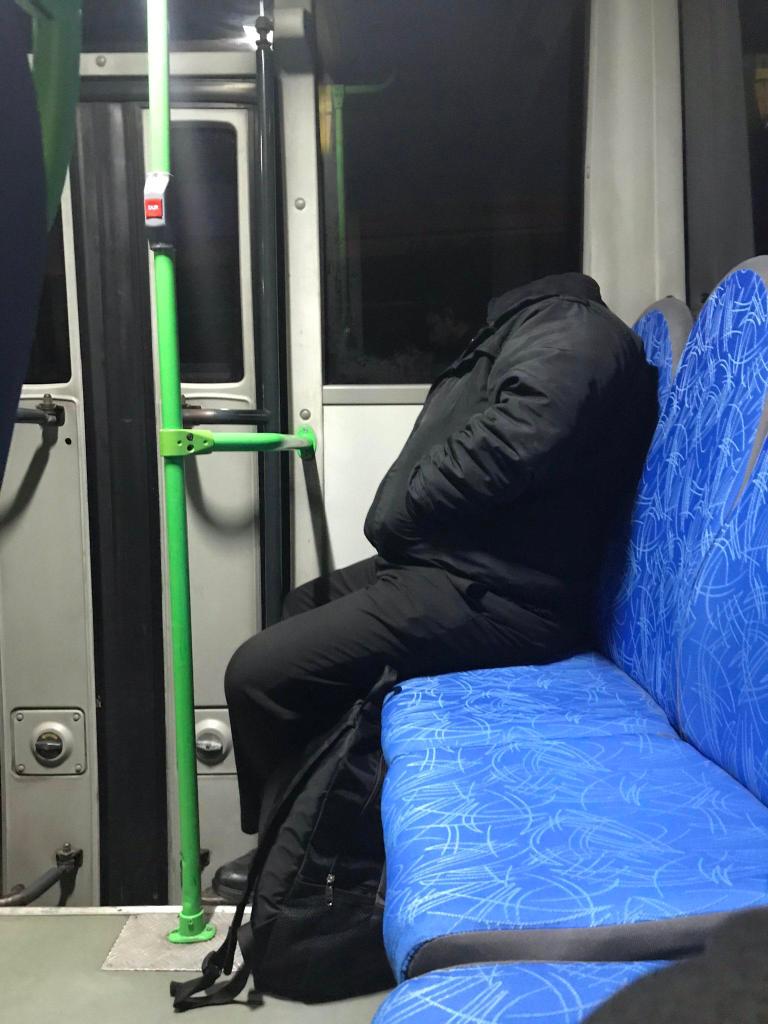 man sitting on bus wearing a black hoodie. His head blends into the black background, so he looks like he is headless.