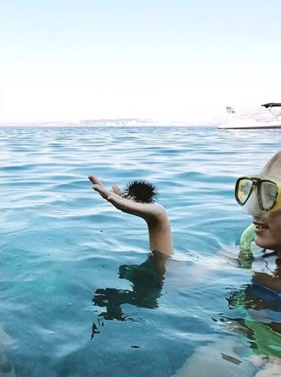 woman holding up a sea urchin, but the angle makes it look like a man with wild hair jumping into the water.