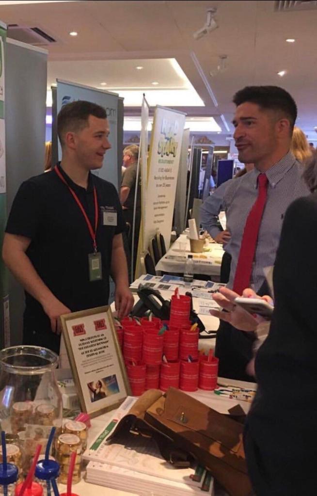 photo of two men at a conference. another man is standing in the background, so it looks like one of the men in the foreground has a tiny arm.