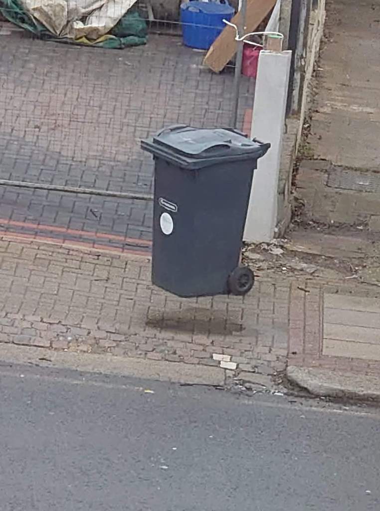 picture of a garbage bin with a wet spot on the pavement nearby, so it looks like the shadow of a floating bin.